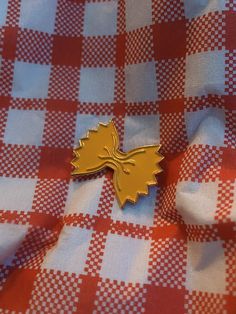 a gold leaf pin sitting on top of a red and white checkered table cloth