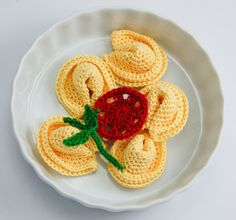 small crocheted fruit on a white plate with green leaves and a red flower