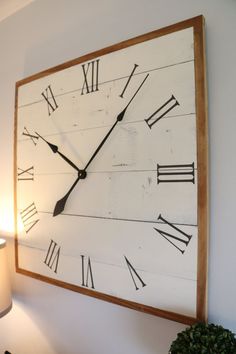 a large clock mounted to the side of a wall next to a lamp and potted plant