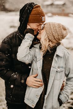 a man and woman standing in the snow with their noses close to each other as they kiss