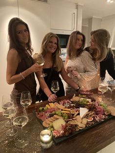 four women standing around a table full of food and wine