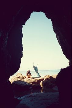 a woman laying on top of a rock covered beach under a blue sky next to the ocean