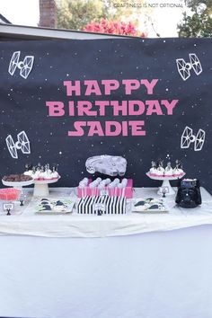 a birthday party table with cakes and cupcakes on it's side, in front of a sign that says happy birthday sadie