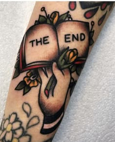 a close up of a person's arm with an open book and flowers on it