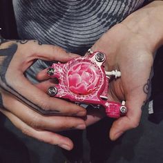 a person with tattoos holding a pink object in their hands and wearing rings on her fingers