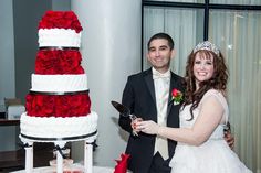 a bride and groom standing next to a wedding cake with red roses on the side