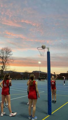 the girls are playing basketball on the court at sunset or dawn, and one girl is jumping up in the air to dunk the ball