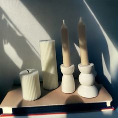 three white candles sitting on top of a table next to two vases and a candle holder