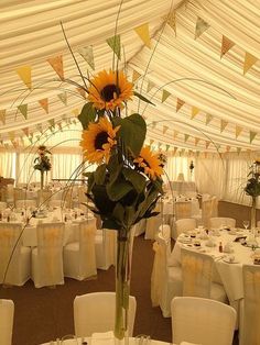 a vase filled with sunflowers sitting on top of a table covered in white clothed tables