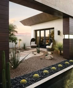 an outdoor living area with cactus, rocks and water in front of the house at sunset