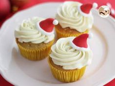 three cupcakes with white frosting and red santa hats on them sitting on a plate