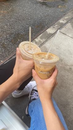 two people holding drinks in their hands on the sidewalk