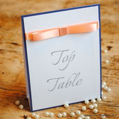 a card with an orange bow on it sitting on a table next to some pearls