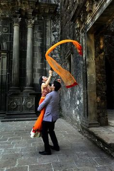 a man and woman standing in front of an old building with orange scarfs around their necks