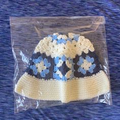 a crocheted hat with blue and white flowers on it sitting in a plastic bag