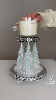 someone is holding a glass candle holder with frosted pine trees on it and silver trimmings