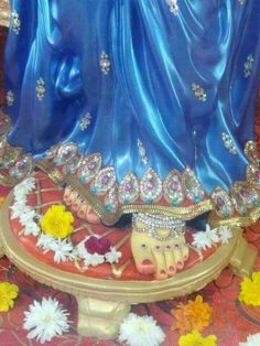 a statue of a woman in blue dress with flowers around her feet on a table