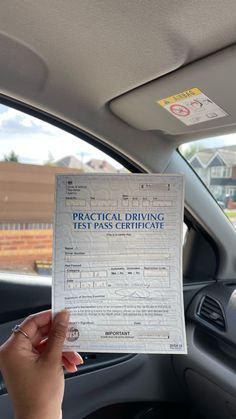 a person holding up a driving test paper in the back seat of a car with their hand on the driver's steering wheel