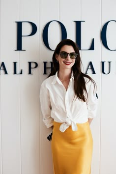 a woman in a white shirt and yellow skirt standing next to a wall with the polo logo on it