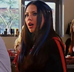 a woman with long hair standing in front of two other women sitting at a table