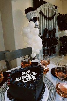 a birthday cake sitting on top of a table with wine glasses and balloons in the background