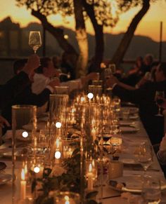 a long table with candles and wine glasses on it at sunset or dusk, in front of a tree