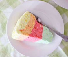 a slice of cake on a white plate with a fork in the middle and three different colors