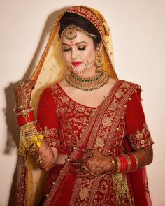 a woman in a red and gold bridal outfit is holding her hands together while looking at the camera