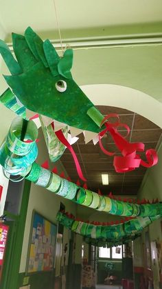 a green dragon hanging from the ceiling in a school hallway with red ribbon and paper streamers