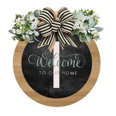 welcome to our home sign with flowers and ribbon on the front, hanging from a wooden plaque