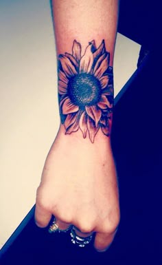 a woman's arm with a sunflower tattoo on it and a hand holding the wrist