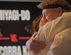 two people hugging each other while standing in front of a sign with words on it