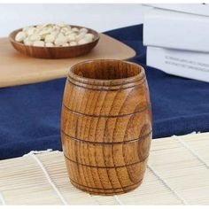 a wooden cup sitting on top of a bamboo mat next to a bowl of nuts