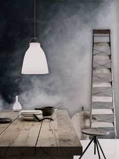 a wooden table sitting under a light next to a tall white lamp hanging from a ceiling