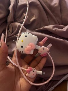 a person holding a hello kitty phone charger in their hand with two cats plugged into it