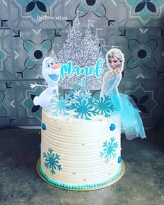 a frozen princess themed cake with frosting and decorations on the top, sitting on a table in front of a wall