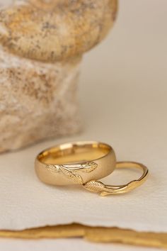 two gold wedding rings sitting on top of a white table cloth next to a rock