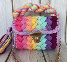 the multicolored braided purse is sitting on a wooden table with a gold chain