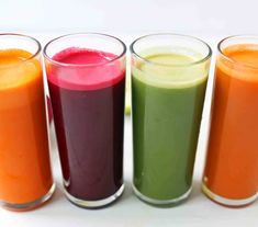 four glasses filled with different colored juices sitting next to each other on a table