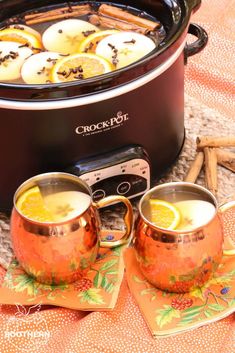 a crock pot filled with lemon slices next to two mugs and cinnamon sticks