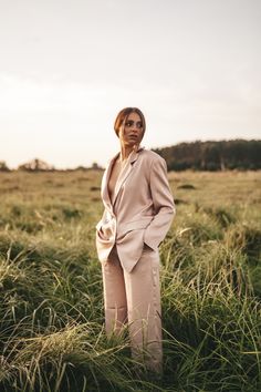 a woman standing in the middle of a field wearing a pink suit and matching heels