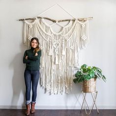 a woman standing in front of a macrame wall hanging