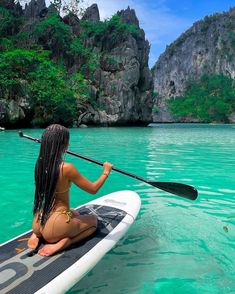 a woman sitting on top of a surfboard in the ocean next to rocks and trees