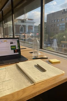 a laptop computer sitting on top of a wooden desk next to a notebook and pen