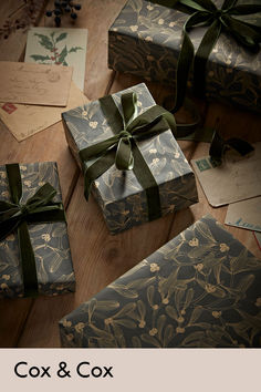 three wrapped presents sitting on top of a wooden table next to envelopes and cards