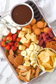 a platter filled with crackers, strawberries, and other snacks next to a bowl of chocolate