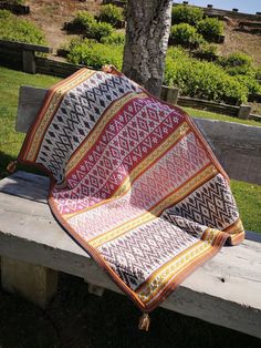 a blanket sitting on top of a wooden bench next to a tree in the grass