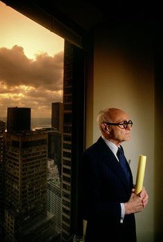 a man in a suit and tie standing next to a window looking out at the city