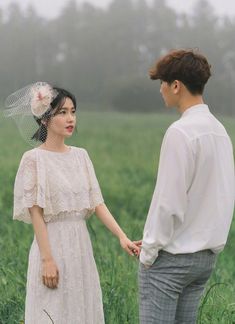 a young man and woman holding hands in a field with foggy sky behind them