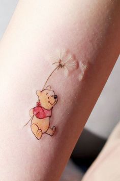 a small winnie the pooh tattoo on the right arm is shown with a dandelion